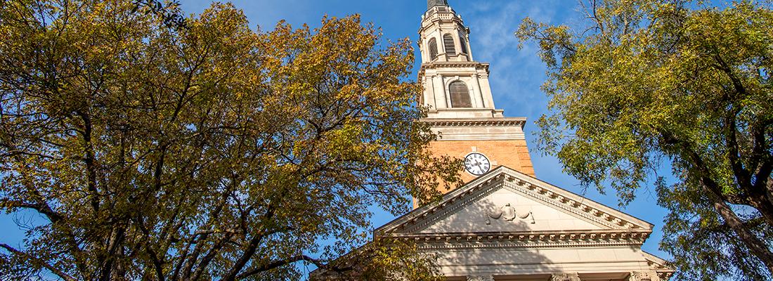 The steeple of the Robert Carr Chapel on the TCU campus, framed by trees and a blue sky.